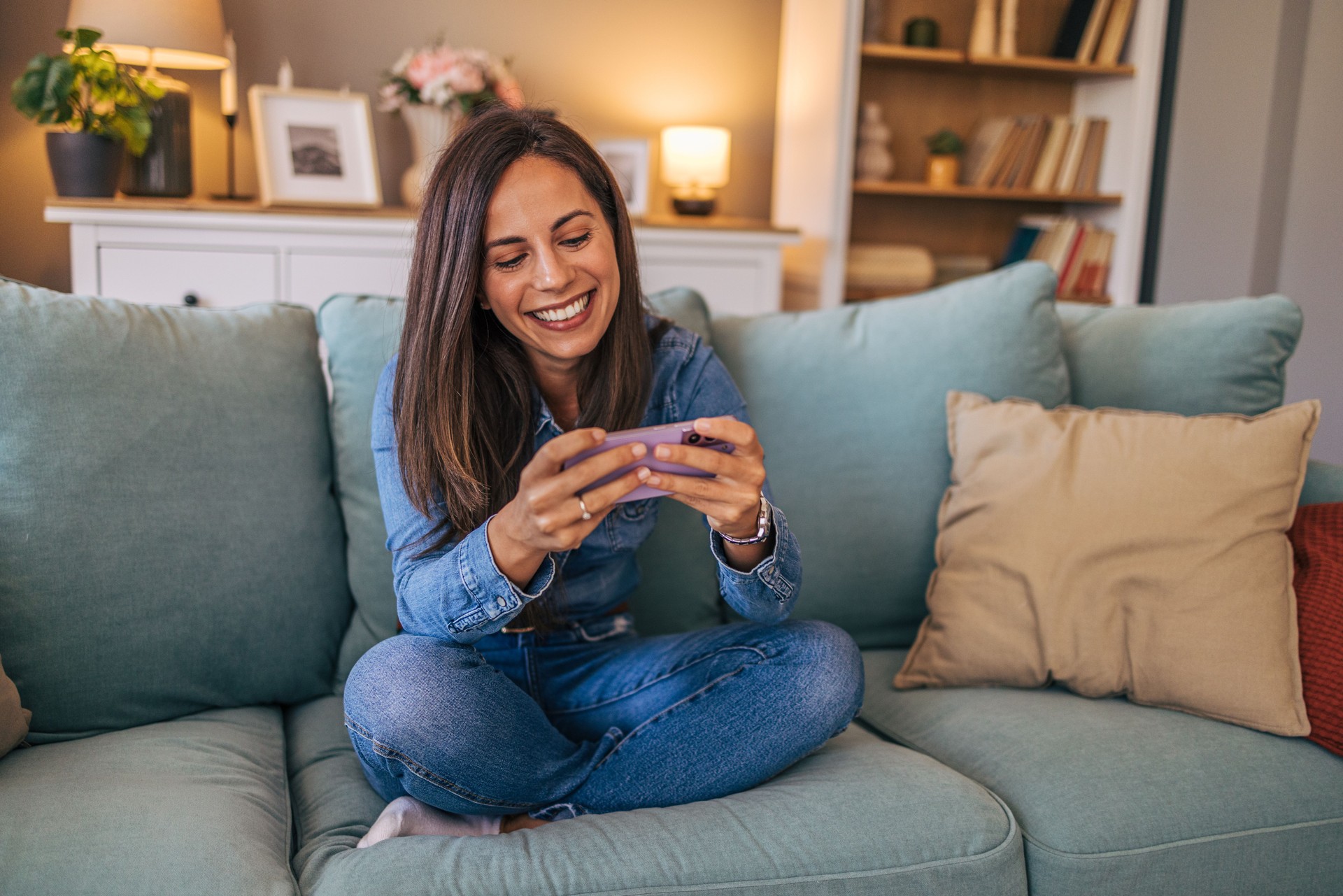 A young cheerful woman sitting on the sofa in the living room and play game on smart phone